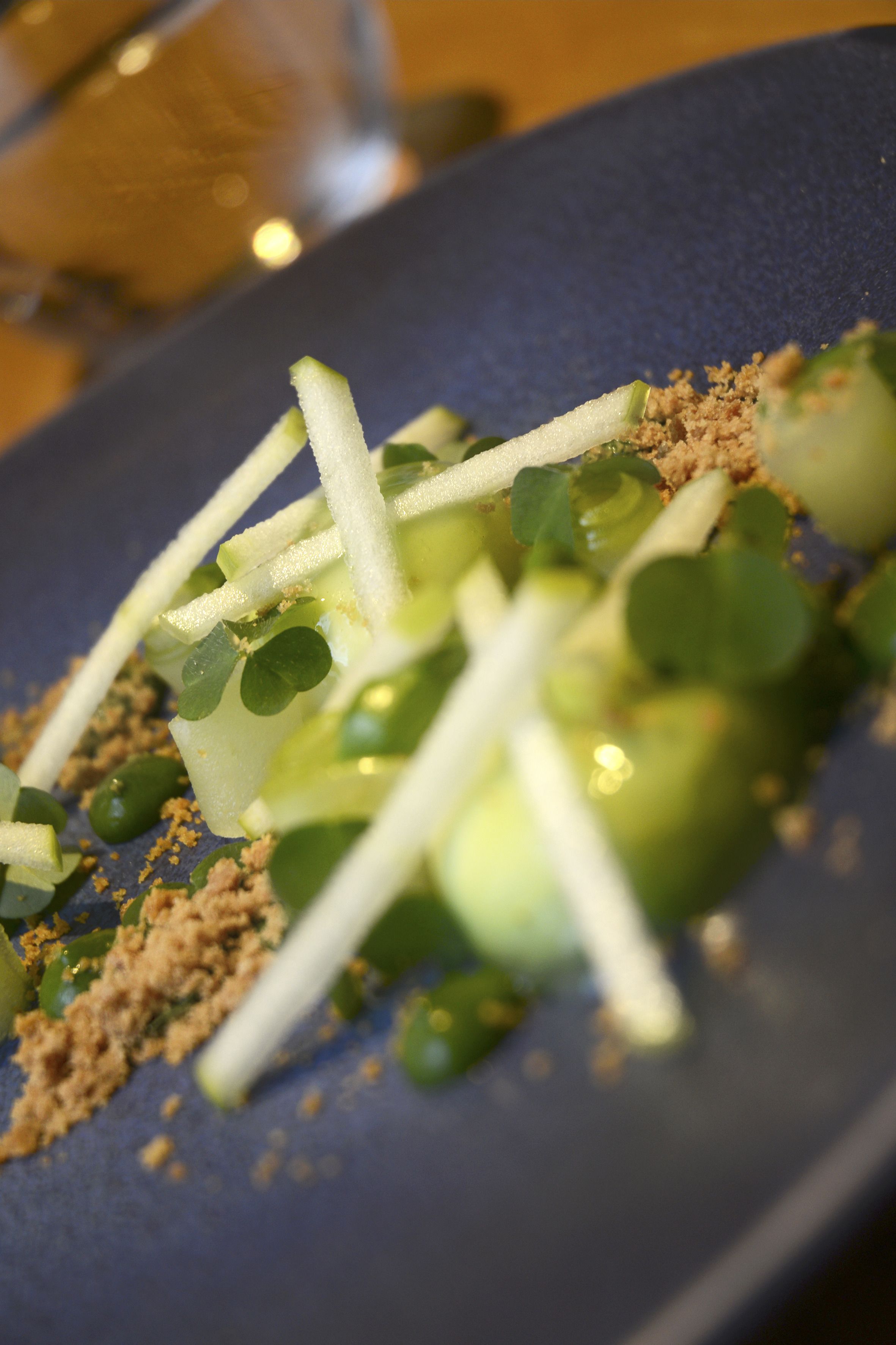 A close-up of a dish with green vegetables and a crumbly topping on a dark plate.