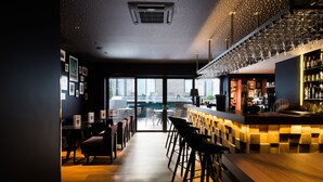 Un área de bar moderna con mostrador, taburetes y vistas a la ciudad a través de amplias ventanas.