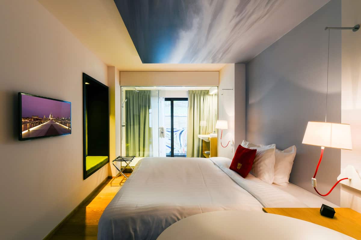 A hotel room with a large bed, a TV mounted on the wall, and a view of the outside through a glass door.