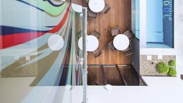Un interior moderno con zona de piscina, suelo de madera y mesas redondas con sillas.