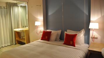 Ein Hotelzimmer mit einem großen Bett, zwei roten Kissen, einem Nachttisch mit Lampe, einem Spiegel und einem Badezimmer mit Waschbecken und Vorhängen.