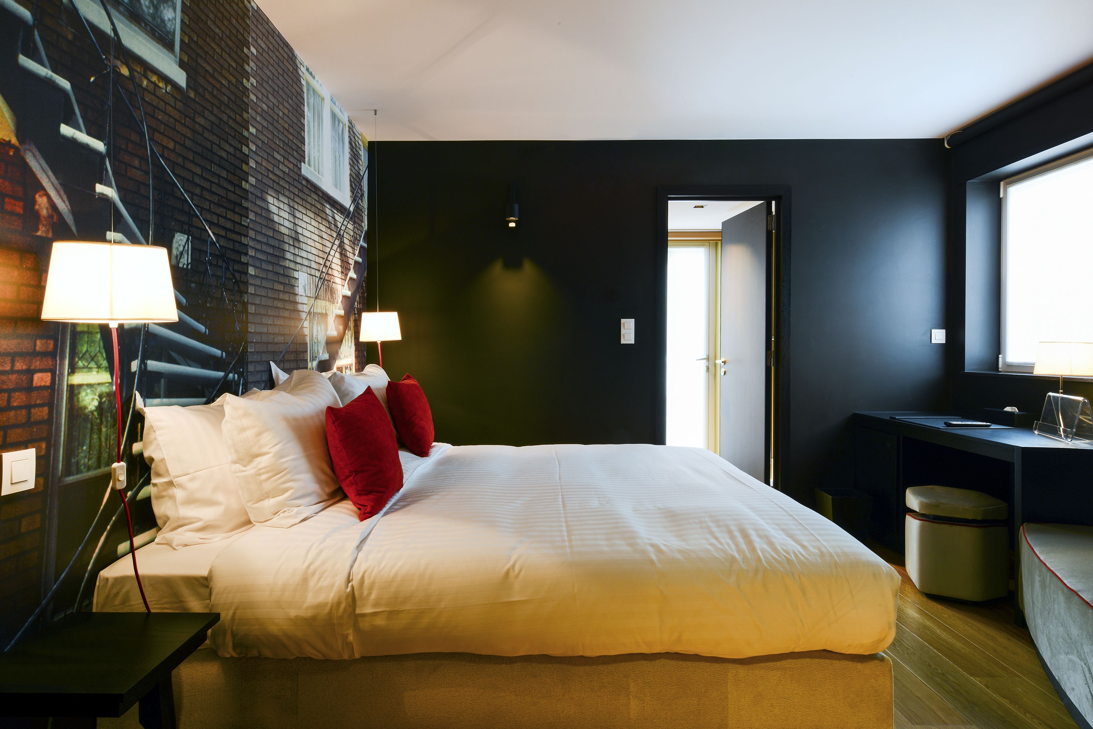 A modern hotel room with a large bed, two bedside lamps, a desk with a chair, and a view of the outside.