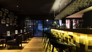 Una zona de bar con suelo de madera, taburetes y una pared con cuadros enmarcados.