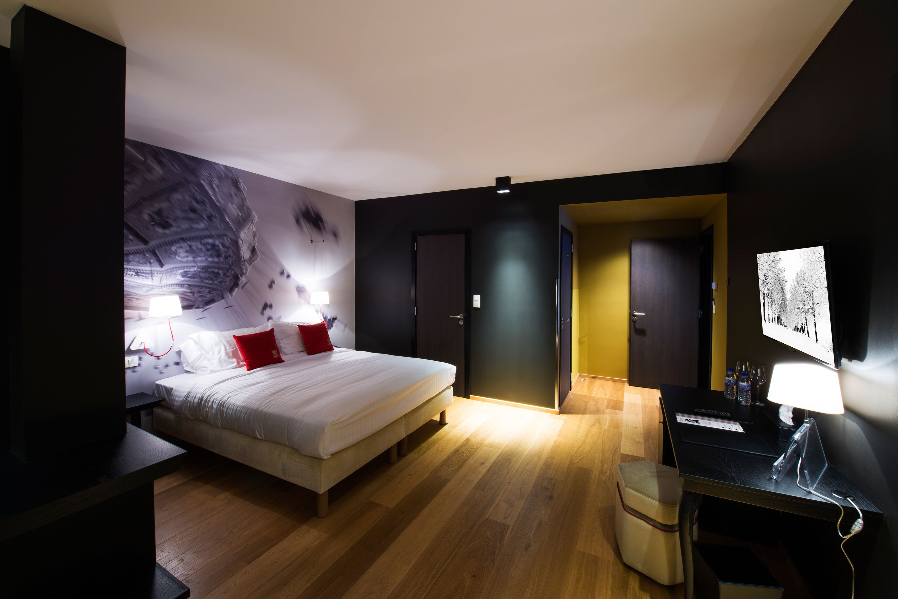 Un dormitorio moderno con una cama grande, un escritorio con computadora y un televisor montado en la pared.