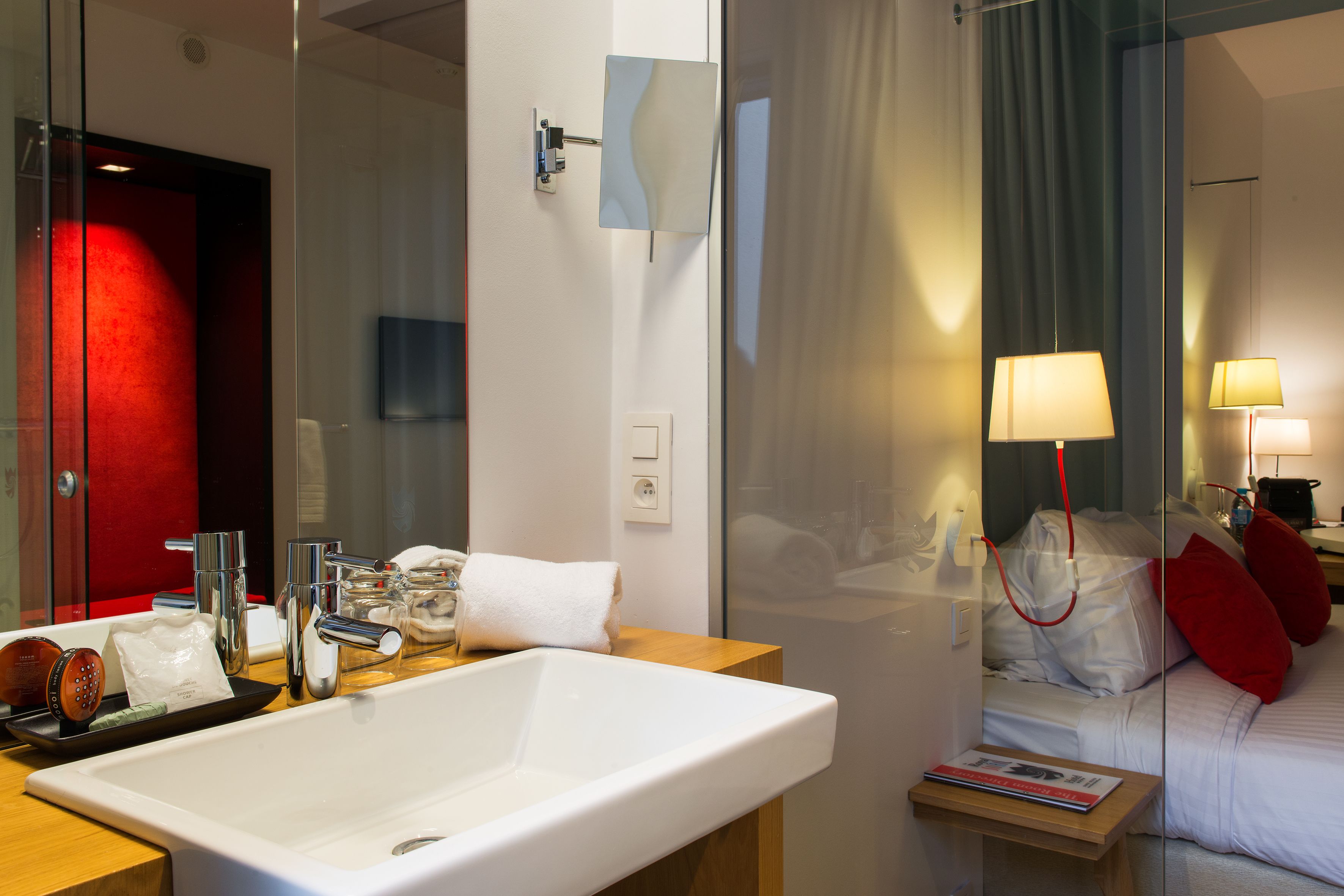 Une salle de bain d’hôtel moderne, dotée d’un grand lavabo, d’un miroir et d’une paroi en verre.