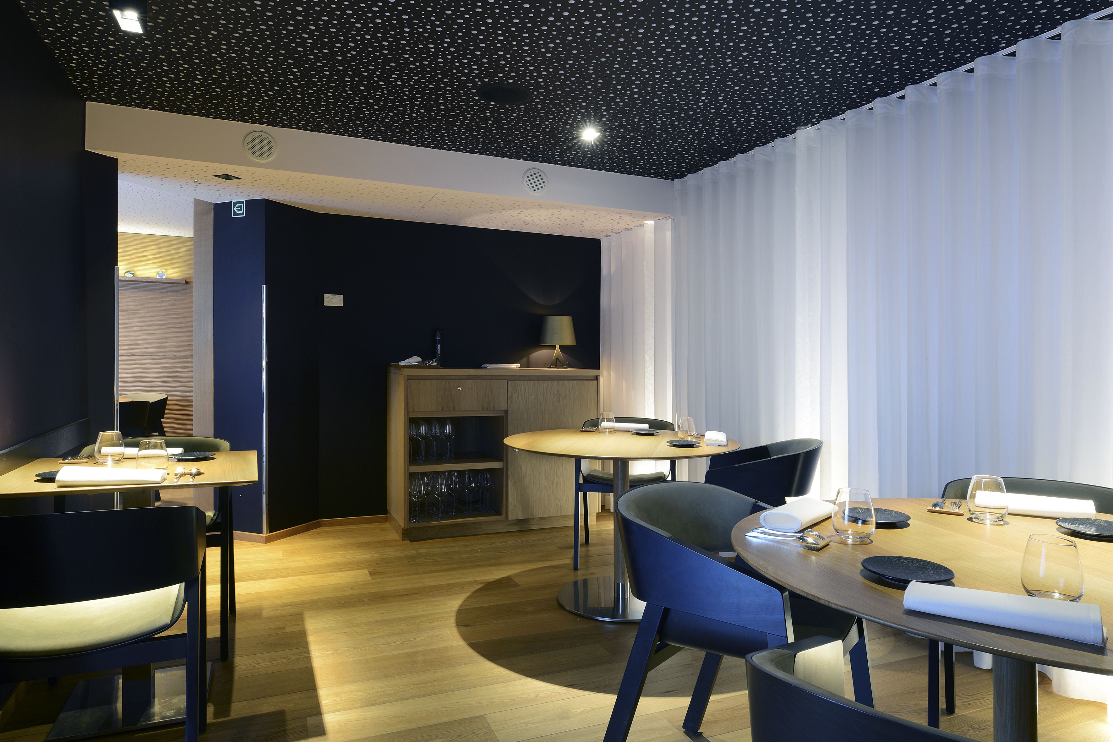 A modern dining area with round tables, blue chairs, and a ceiling with a starry pattern.