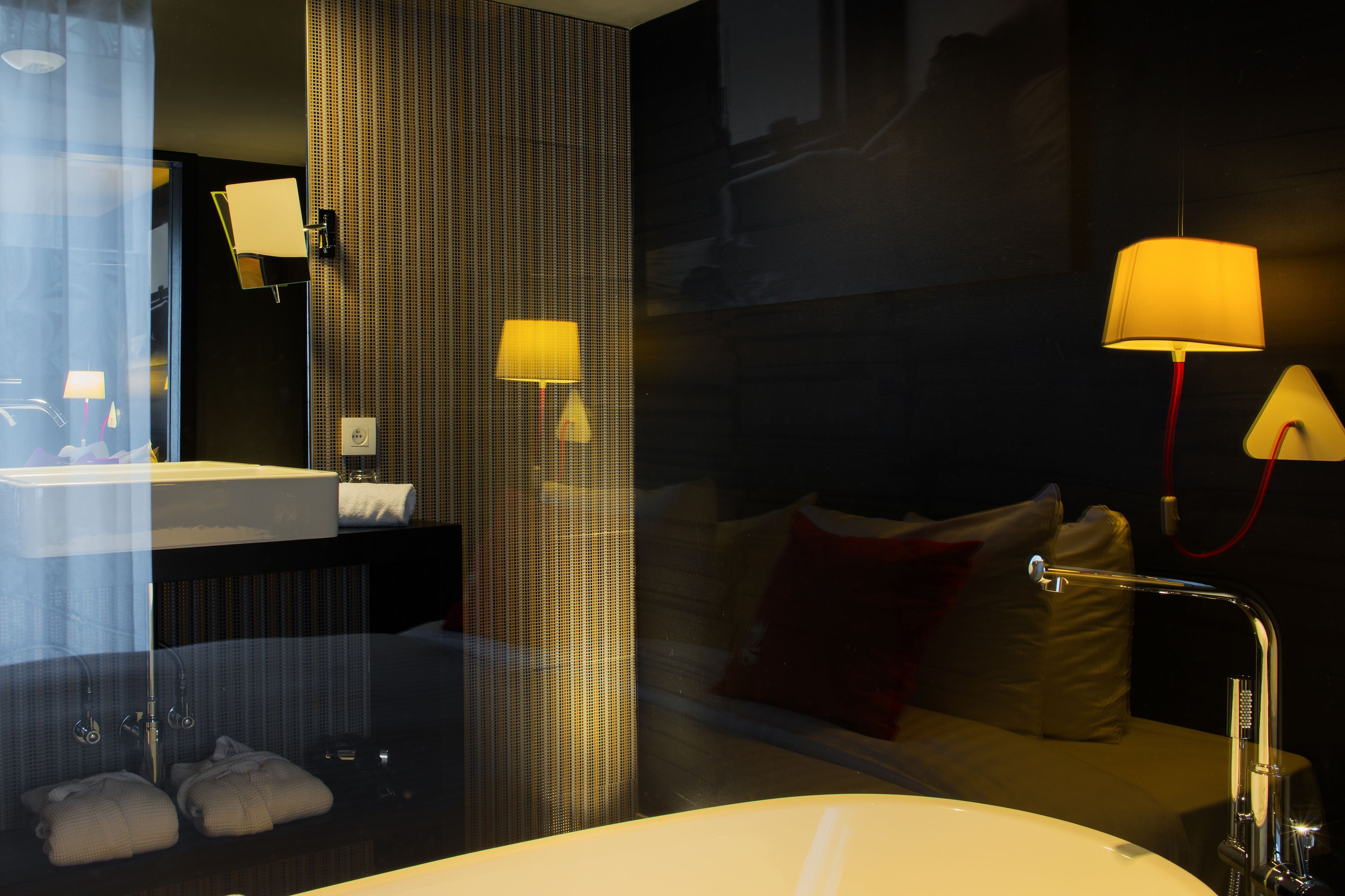 Ein Hotelzimmer mit einer großen weißen Badewanne, einem Spiegel, einem Bett mit Kissen und zwei Wandleuchten.