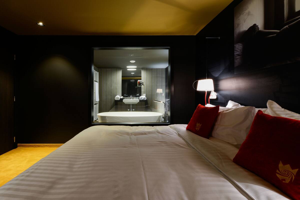 A hotel room with a large bed, a bedside lamp, and a view of the bathroom.