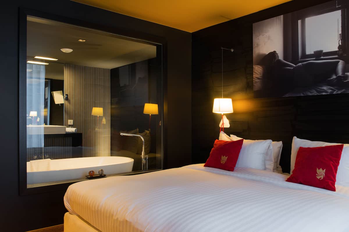 A hotel room with a large bed, a bathroom with a bathtub, and a large mirror.