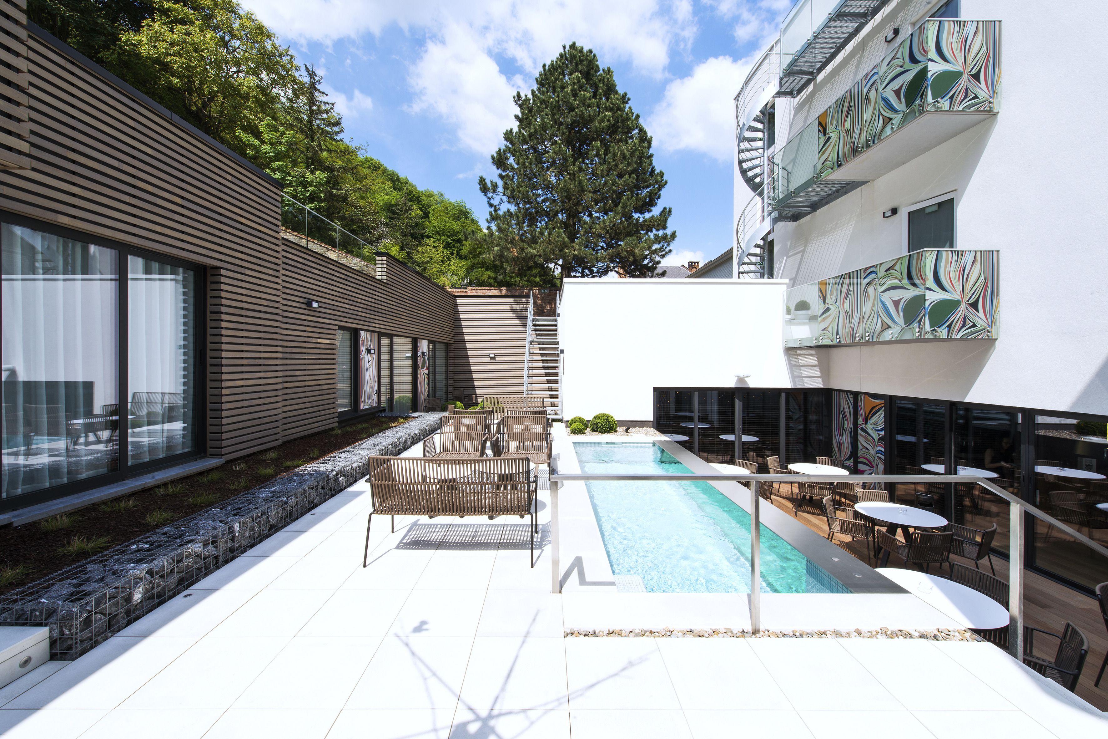 A modern outdoor pool area with seating and a staircase leading to a building.