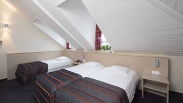 Een hotelkamer met een schuine plafond, twee bedden met donkere en lichte beddengoed, een nachtkastje, een klein raam met gordijnen en een wandlamp.