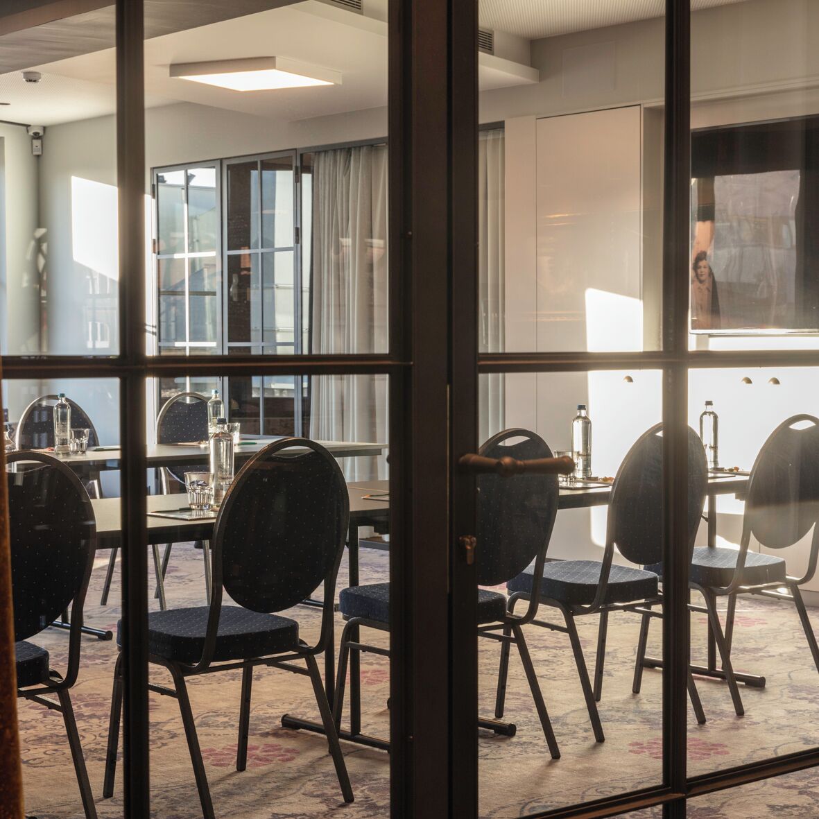 Un salón de conferencias con mesas y sillas, ventanas amplias y vistas al exterior.