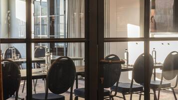 Un salón de conferencias con mesas y sillas, ventanas amplias y vistas al exterior.