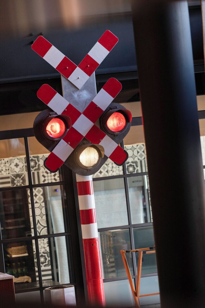 A red and white railway crossing sign with two illuminated lights.