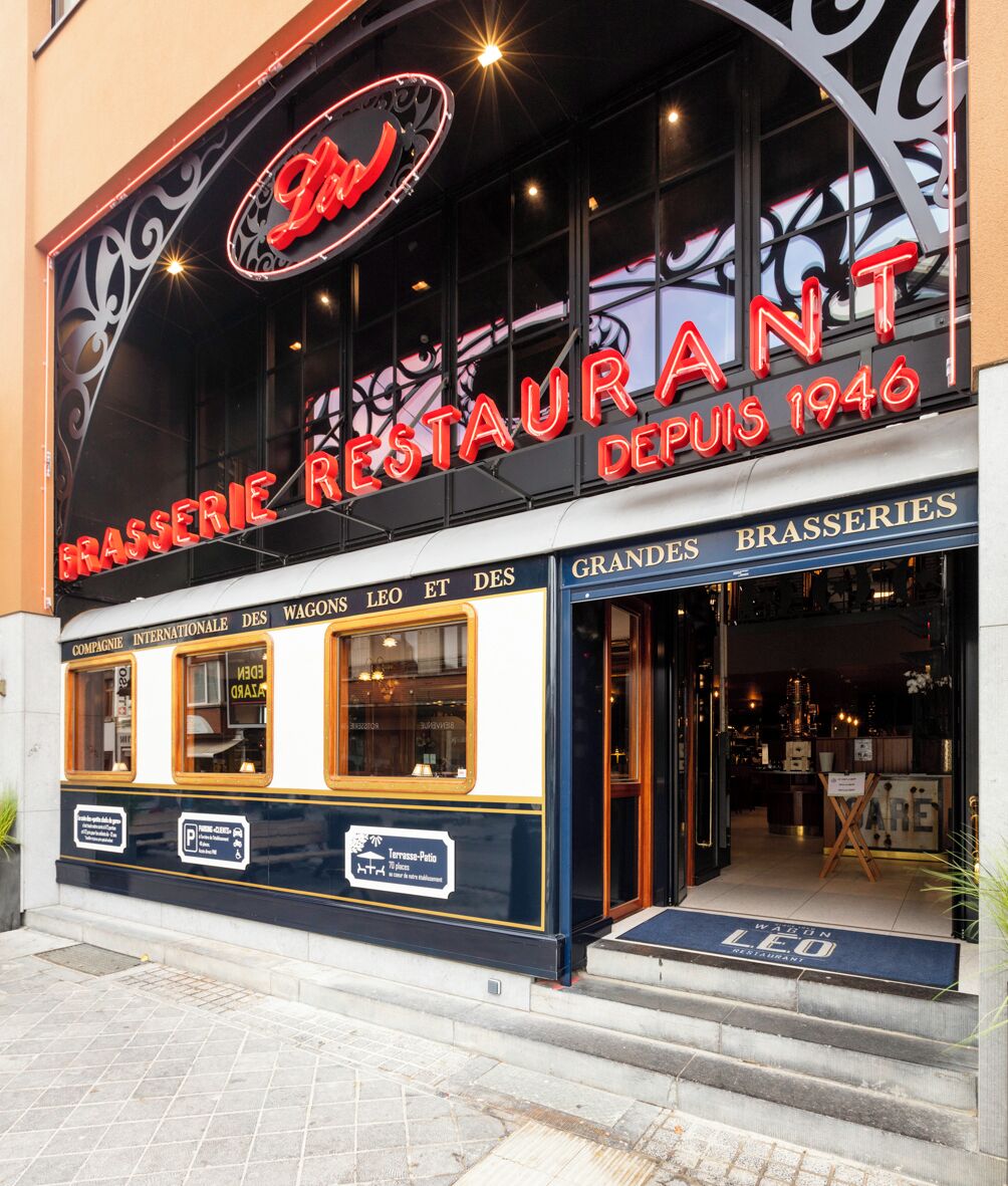 Un restaurant avec une enseigne au néon, un auvent noir et une entrée bleue.