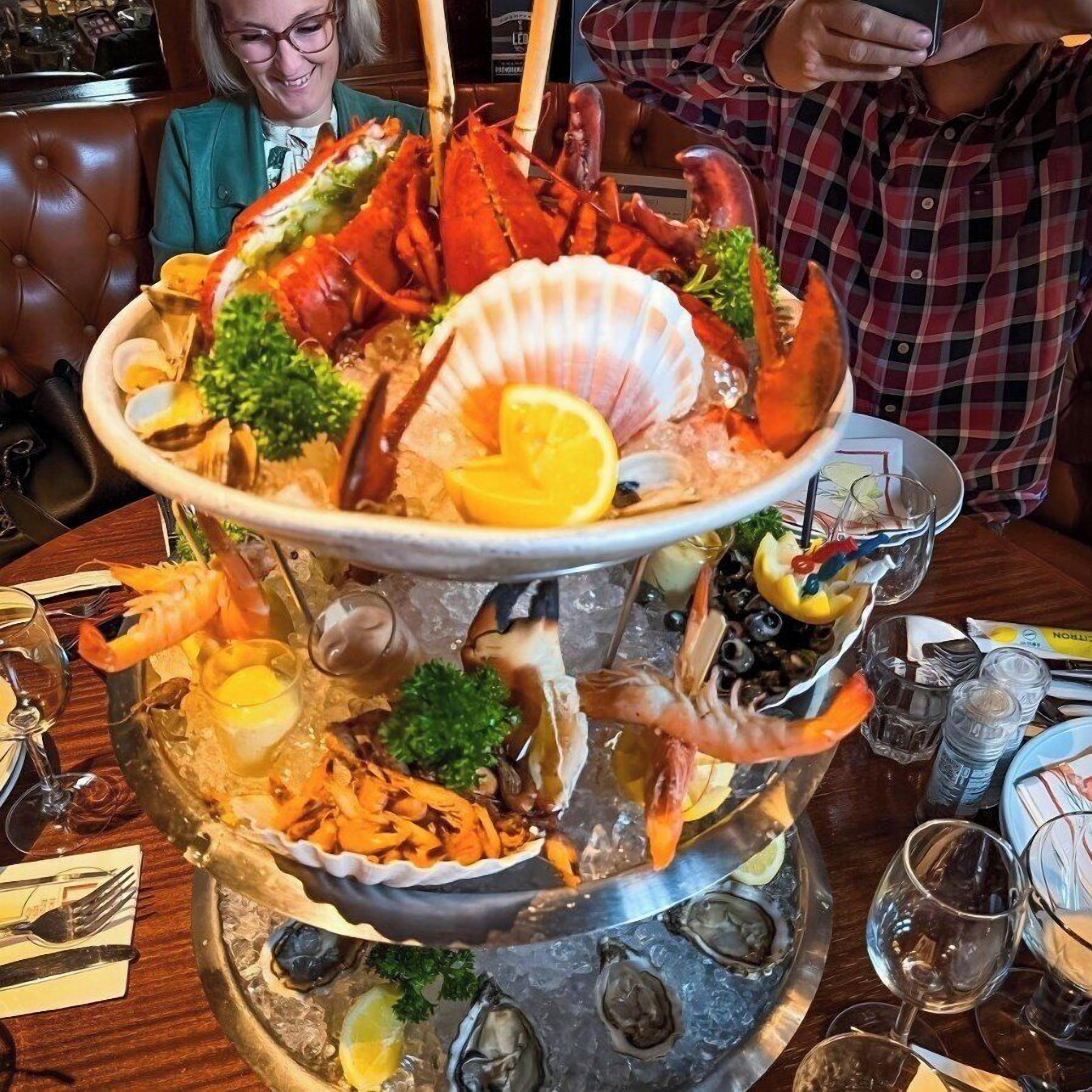 Un plato de mariscos con diversos moluscos y un vongole sobre una base de hielo, rodeado de vasos y cubiertos en una mesa.