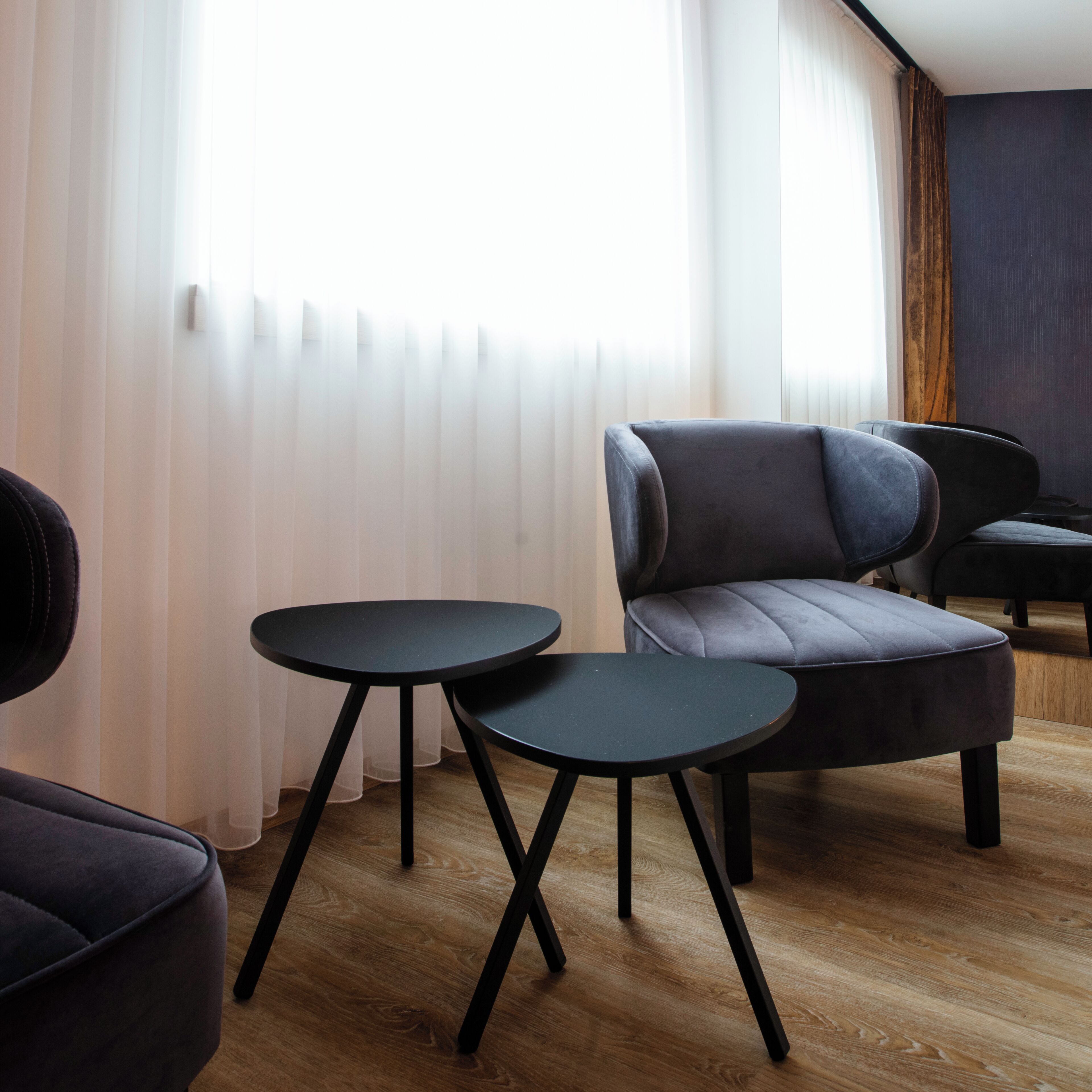 A modern living room with a sofa, two small tables, and a window with sheer curtains.