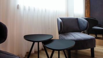 Una sala moderna con un sofá, dos mesitas y una ventana con cortinas translúcidas.