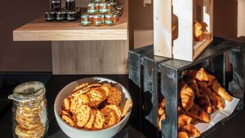 En træhylde med syltetøjsglas, en skål med småkager og et udstilling af croissanter i en trækasse.