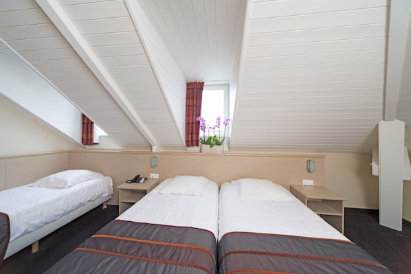 A hotel room with two single beds and a larger bed, a small table with a phone, a nightstand, and a window with curtains. - Hotel Leo Station et Annexes (Bastogne)