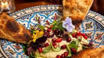 Een bord met een salade, granaatappelpitjes en een stuk brood.