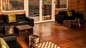 Amplia habitación con piso de madera, sofá de cuero negro, mesa de centro de madera y un tablero de ajedrez.