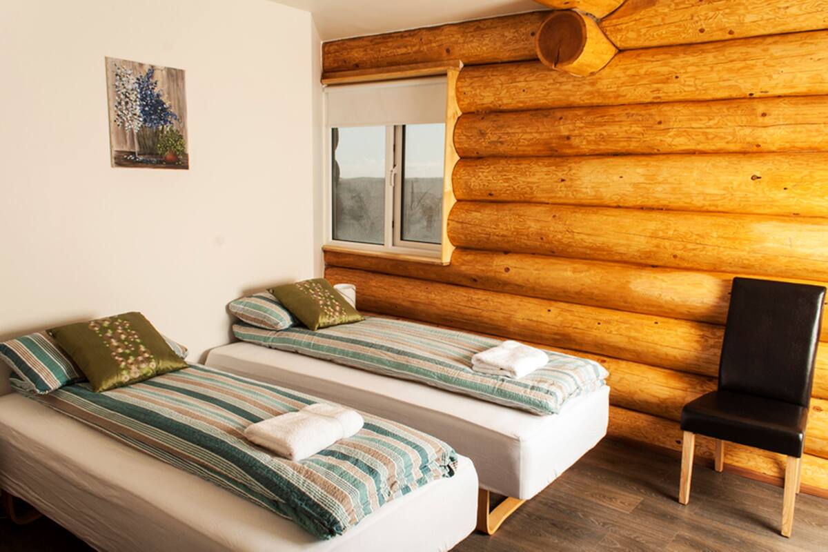 Una habitación con dos camas, paredes de madera, una ventana y una silla.