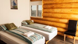 Una habitación con dos camas, paredes de madera, una ventana y una silla.