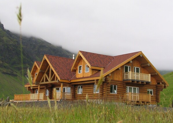 A wooden log cabin with a red-tiled roof, multiple balconies, and a grassy foreground. - Welcome Lambafell (Rangárþing eystra)