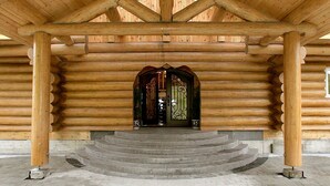 Una cabaña de troncos con una entrada central, una puerta decorativa y una escalera que lleva hacia ella.