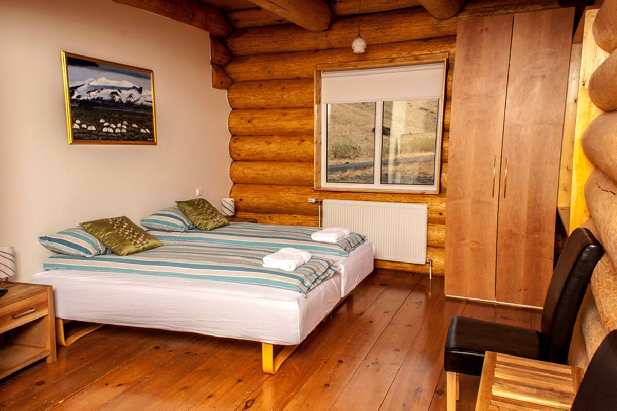 Un dormitorio tipo cabaña de troncos con una cama, paredes de madera, una ventana y un cuadro.