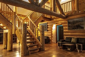 A log cabin interior with a wooden staircase, a living area with a sofa and ottoman, and a large framed picture on the wall. - Welcome Lambafell (Rangárþing eystra)