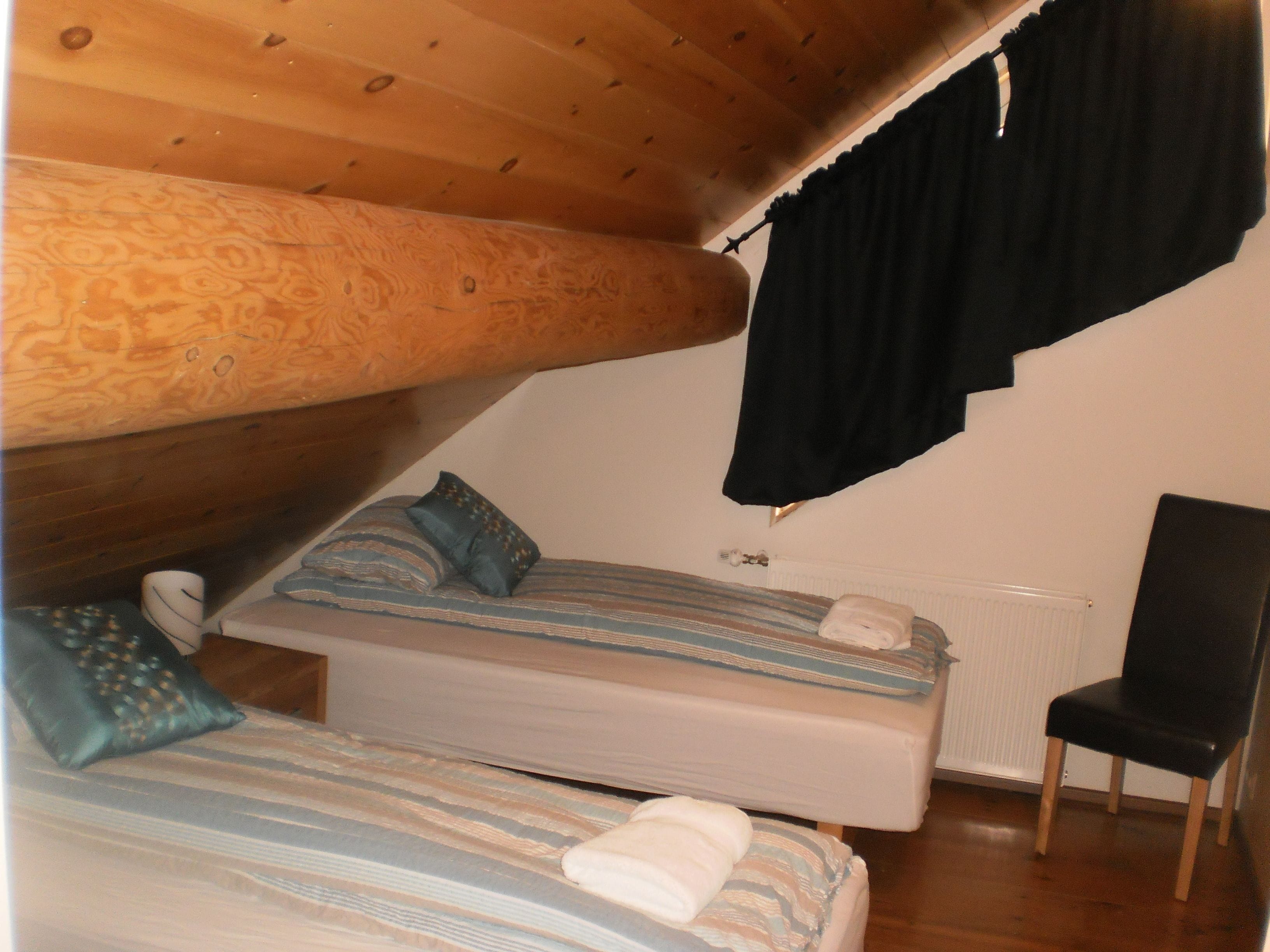 A small, cozy room with two beds, a chair, and a radiator.
