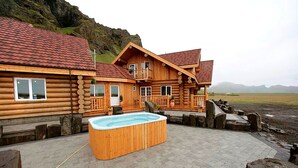 Una cabaña de troncos con jacuzzi, terraza de madera y vistas al paisaje.