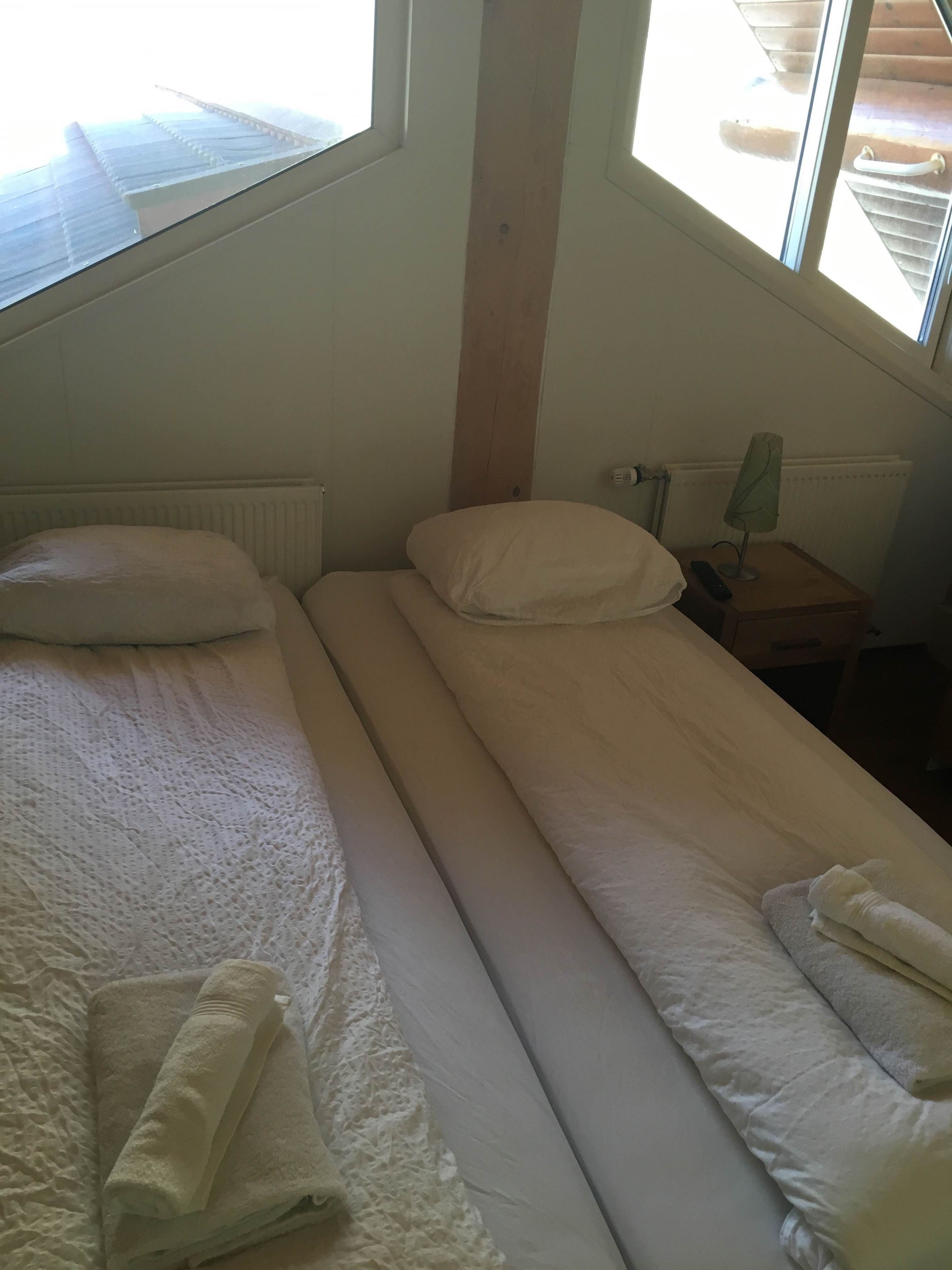 A small, single-bed room with a window, a bedside table with a lamp, and a radiator.