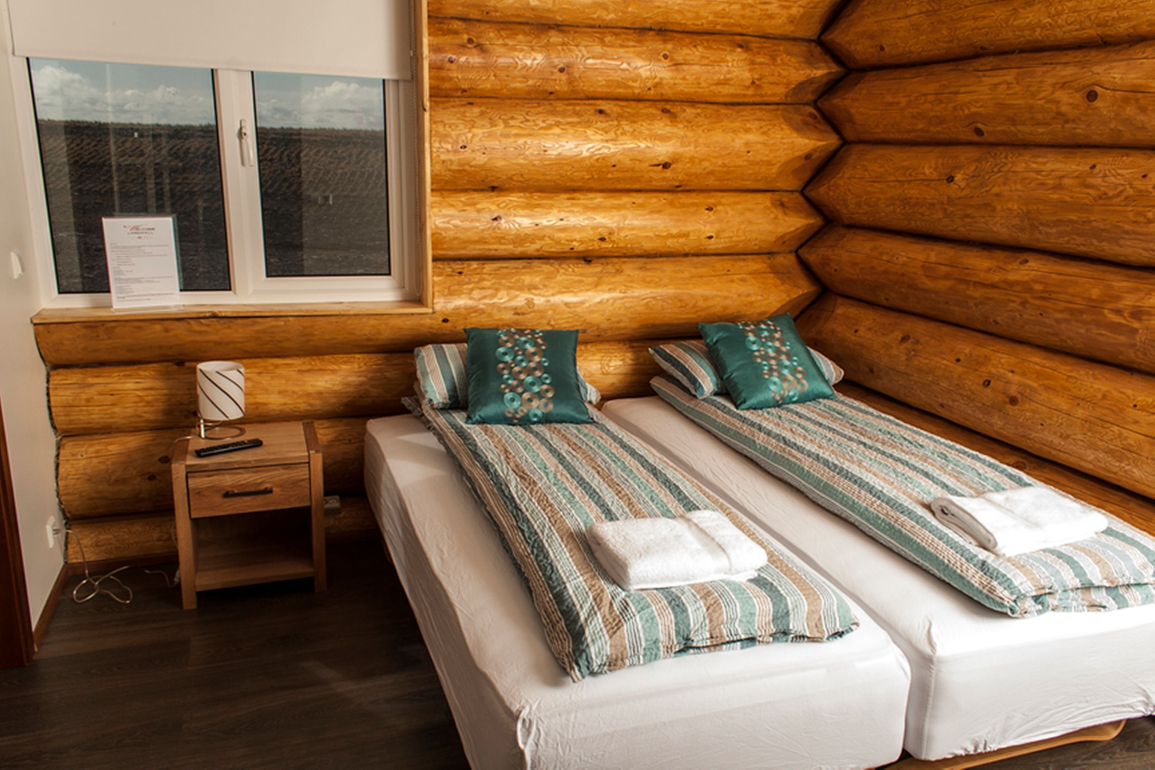 A log cabin room with two beds, a nightstand, and a window.