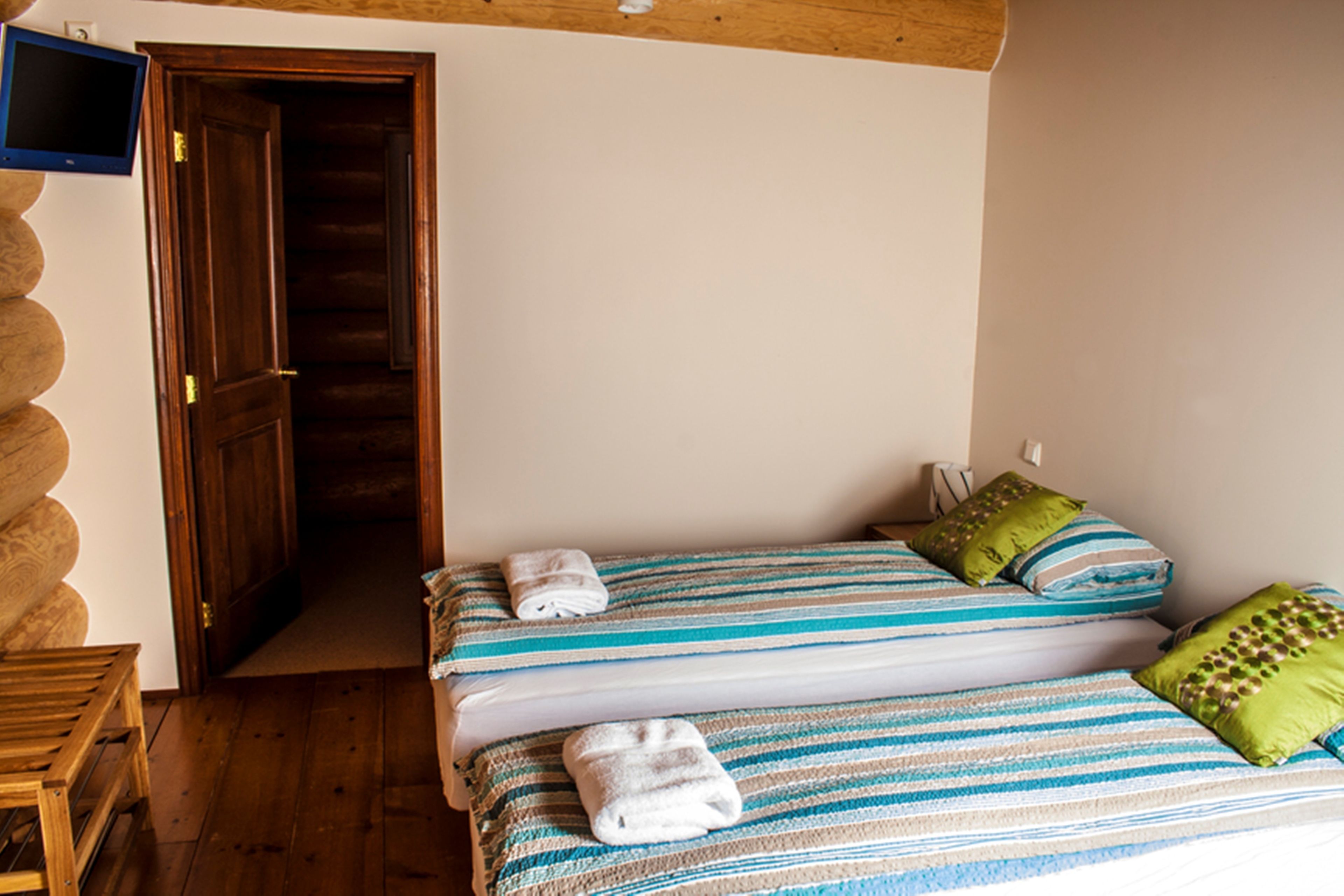 A room with two beds, wooden flooring, a television on the wall, and a wooden door.