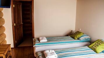 A room with two beds, wooden flooring, a television on the wall, and a wooden door.
