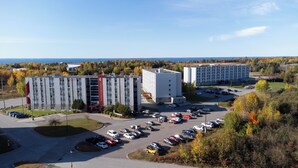 A multi-story parking garage with a red and white building adjacent to it, surrounded by autumn foliage and a clear sky. - Residence & Conference Centre - North Bay (North Bay)