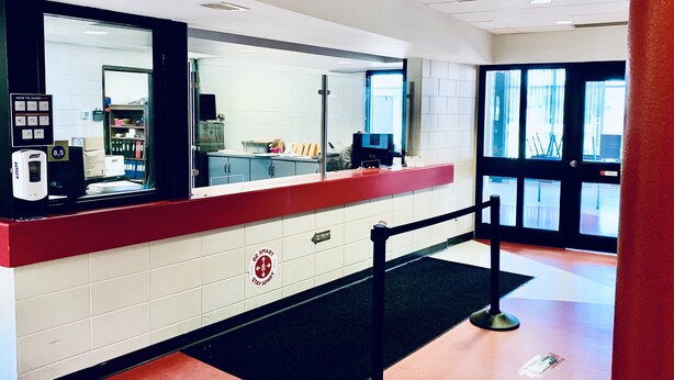 A reception area with a red counter, a black security barrier, and a sign that reads "BE SMART STAY APART". - Residence & Conference Centre - North Bay (North Bay)