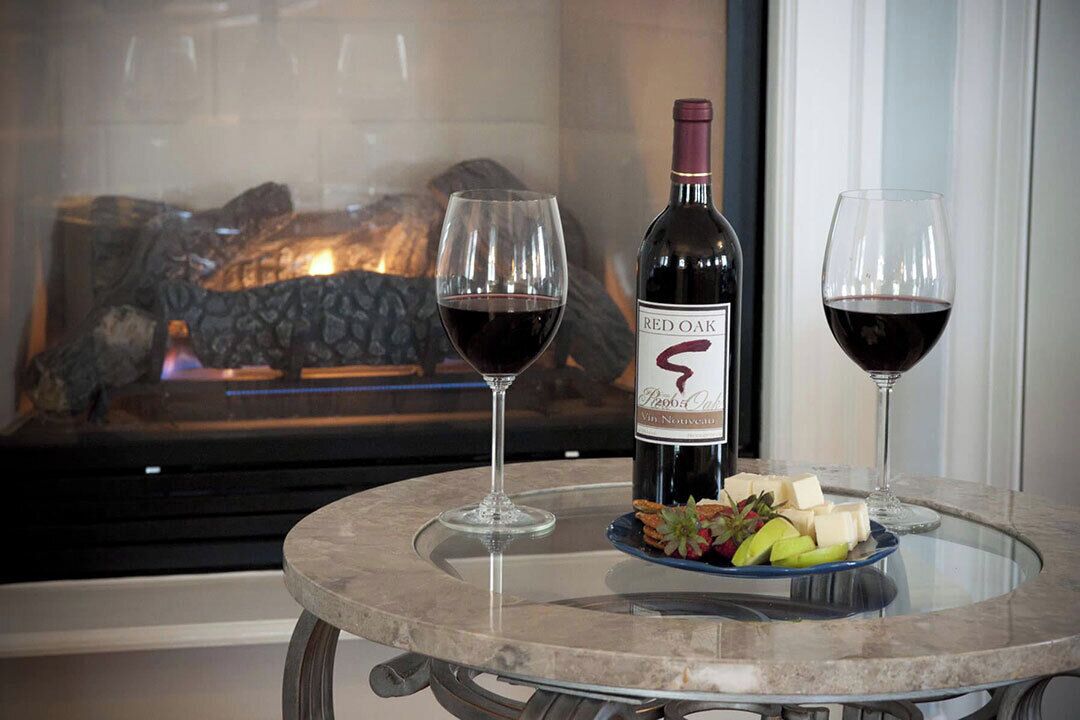 A glass table with a bottle of Red Oak wine, two glasses of wine, and a plate of cheese and fruit.