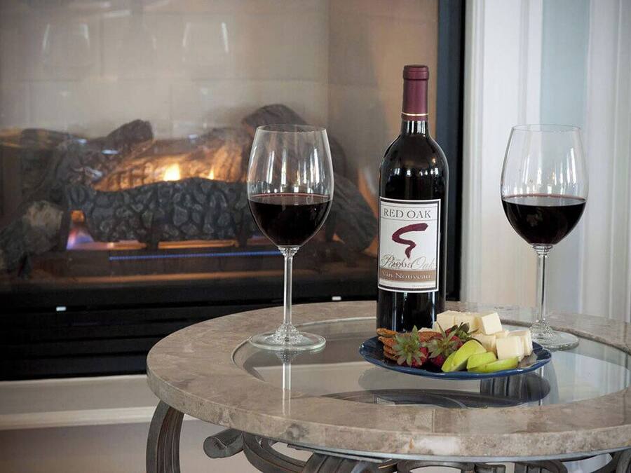 A glass table with a bottle of Red Oak wine, two glasses of wine, and a plate of cheese and fruit.