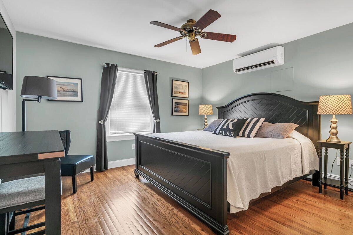 A bedroom with a bed, a desk, a chair, a ceiling fan, and an air conditioning unit.