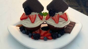 Un postre en un plato blanco con fresas, moras y una barra de chocolate.