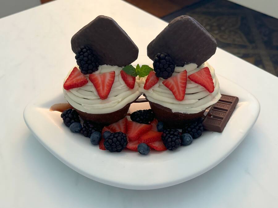 Un postre en un plato blanco con fresas, moras y una barra de chocolate.