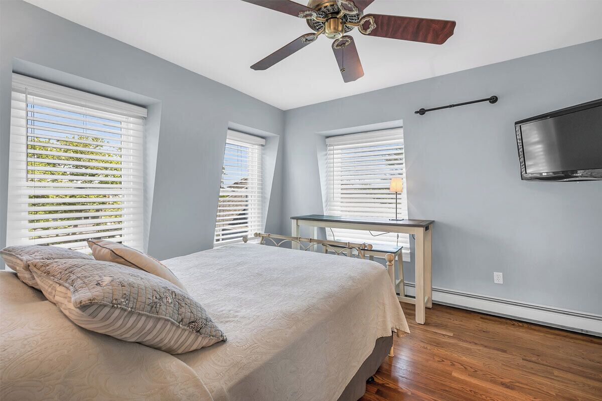 Une chambre à coucher avec un lit, un ventilateur de plafond et un téléviseur fixé au mur.