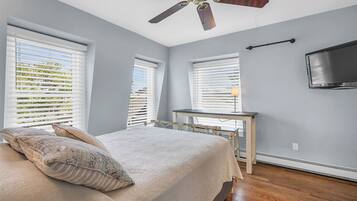 Une chambre à coucher avec un lit, un ventilateur de plafond et un téléviseur fixé au mur.