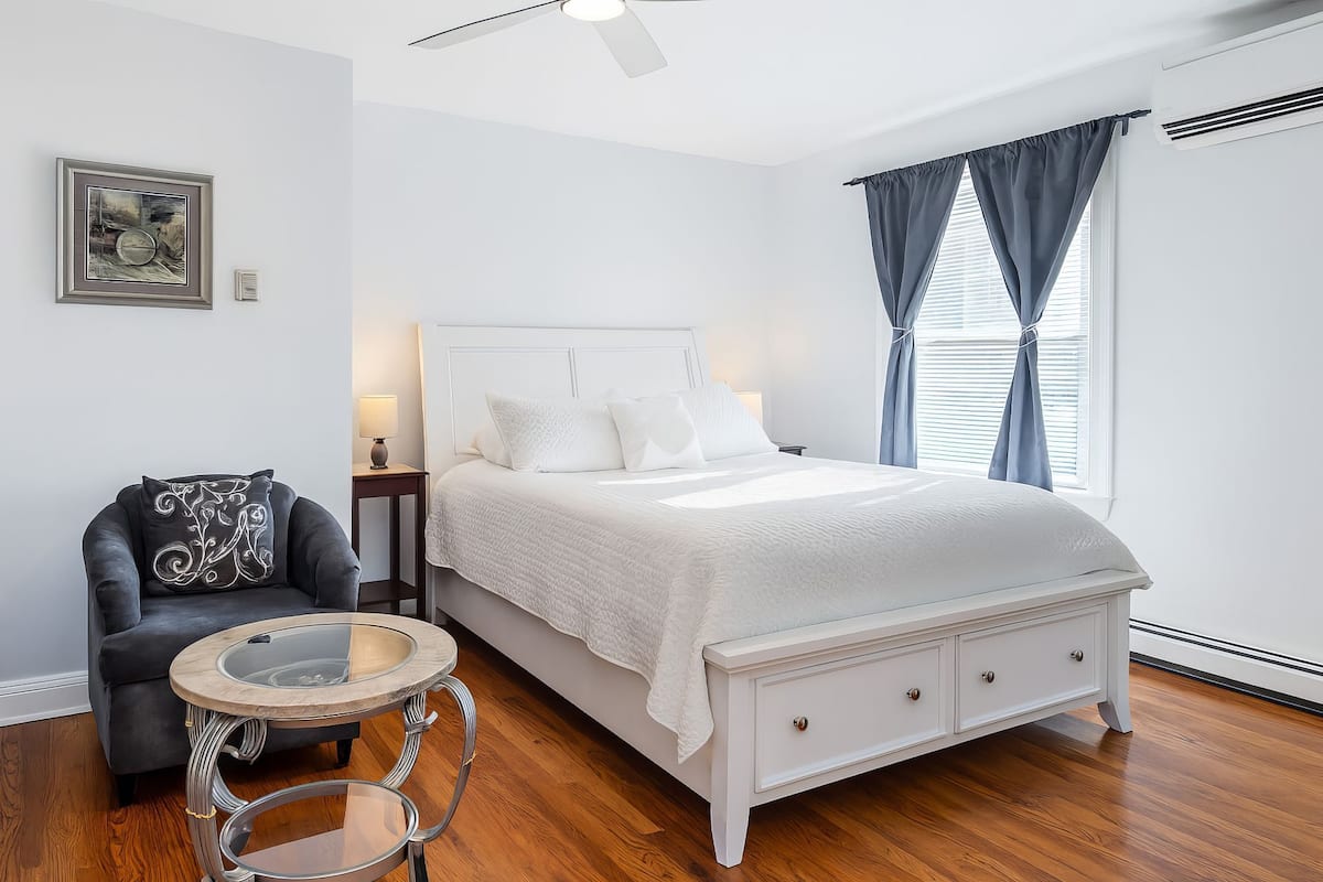 A bedroom with a bed, a chair, a round table, and a painting on the wall.