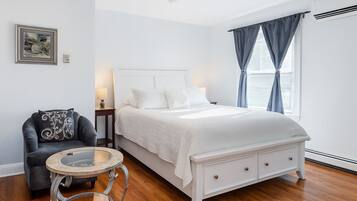 A bedroom with a bed, a chair, a round table, and a painting on the wall.