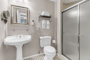 Un baño con lavamanos pedestal, inodoro, cabina de ducha, toallero y espejo con marco dorado.